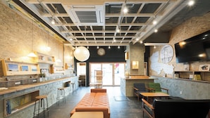 A modern interior with a long wooden bench, bar stools, and a seating area with a black couch. - Kotori Coworking and Hostel Kotohira (Kotohira)