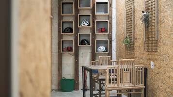 A room with a wooden table and chairs, a green bucket, and shelves with helmets and red cups.