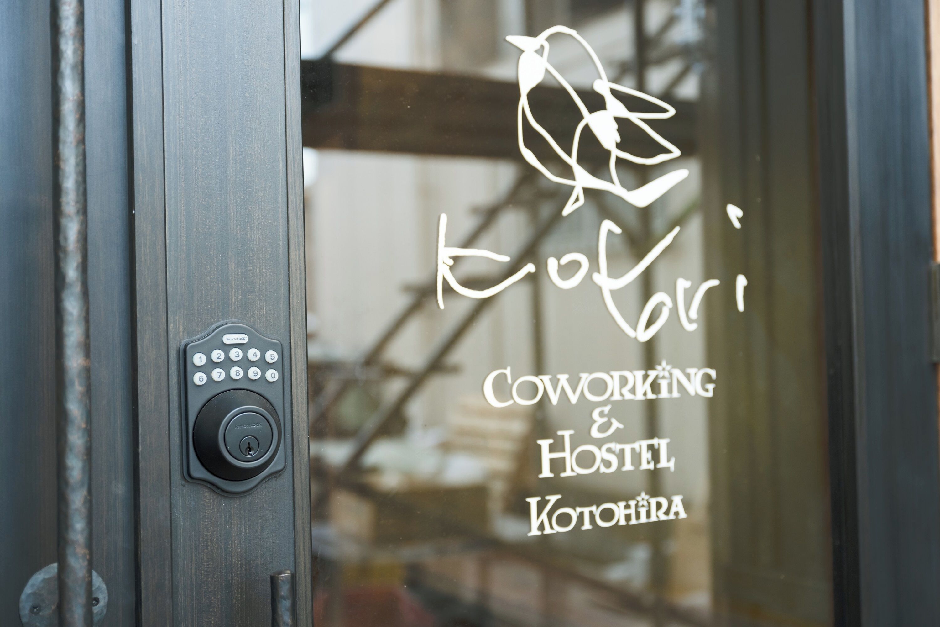 Uma fechadura eletrônica em uma porta com janela exibindo o texto "Coworking & Hostel Kotohira".