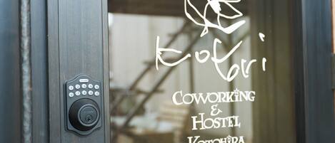 A keypad lock on a door with a window displaying the text "Coworking & Hostel Kotohira".