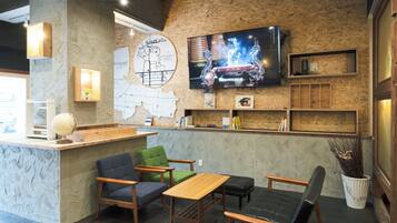 A cozy cafe with a wooden counter, comfortable seating, a flat-screen TV, and a decorative wall.