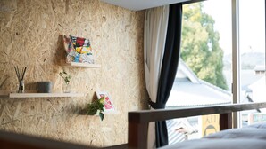 A room with a wooden wall, a window with curtains, and a bed. - Kotori Coworking and Hostel Kotohira (Kotohira)