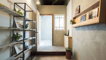 A hallway with a wooden door, a small window, and shelves with plants and books.