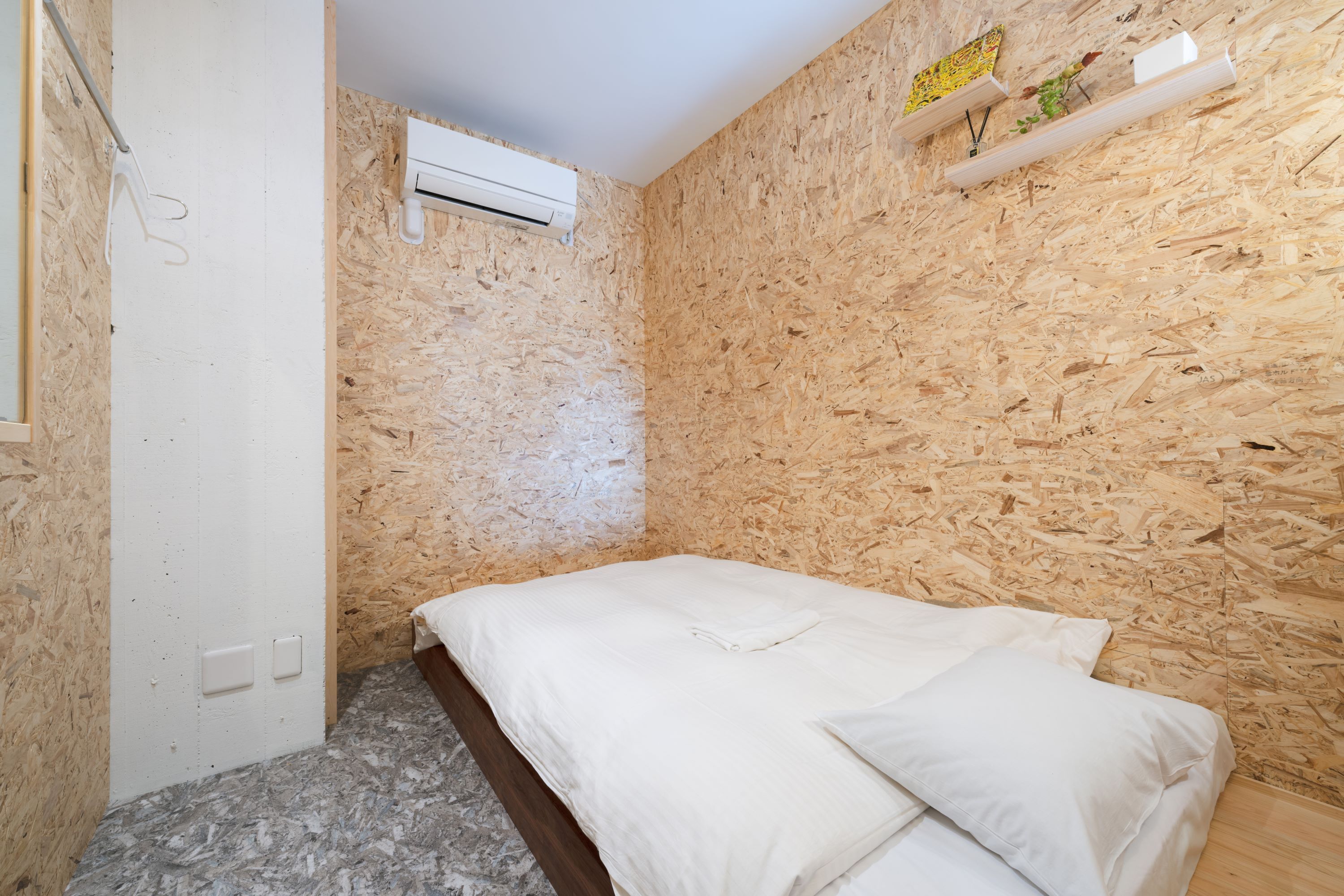 Una habitación pequeña y acogedora con cama, paredes de madera, un equipo de aire acondicionado y un estante con adornos.