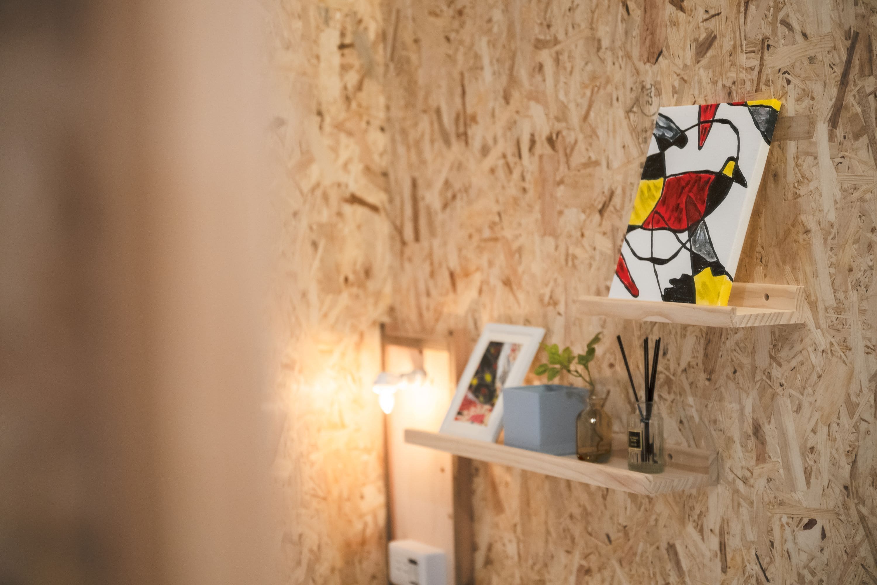 Een houten wand met een lijstwerk en een plank waarop een plant en een klein vaasje staan.