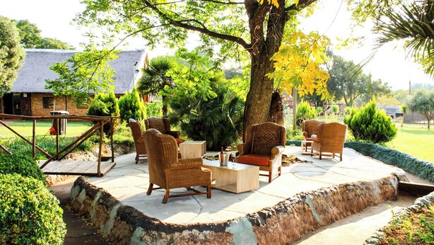 An outdoor seating area with wicker furniture, a table, and a large tree. - Biko's Villa (Magaliesberg)