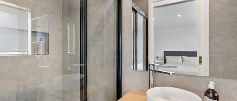 A modern bathroom with a glass shower enclosure, a white sink, and a mirror above it.