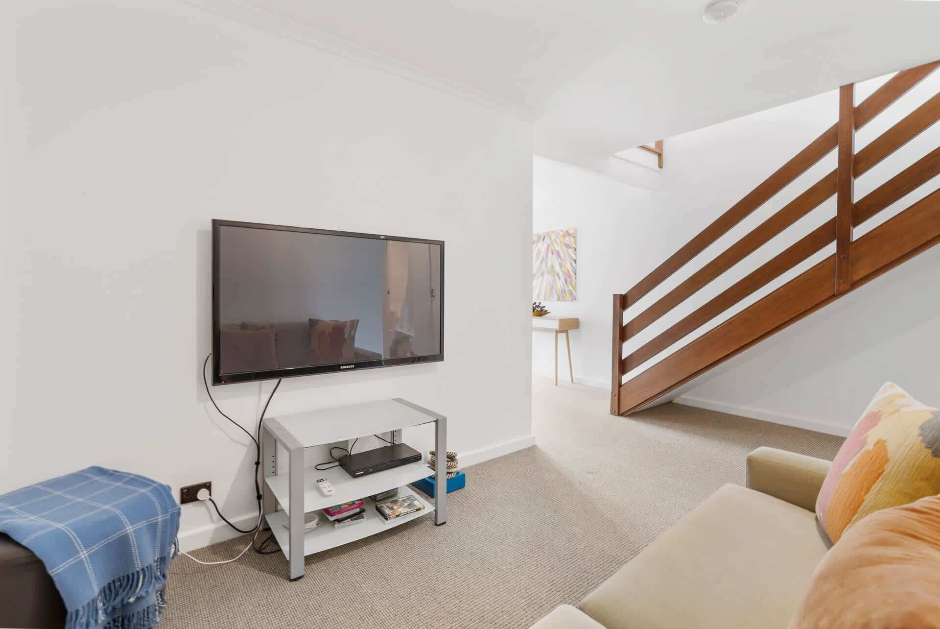 A living room with a flat-screen TV, a white entertainment unit, a sofa, and a staircase.