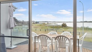 Un balcon avec une table et des chaises, une vue sur un lac et un espace verdoyant agrémenté d’un pavillon.
