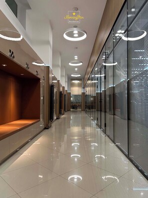 A modern hotel corridor with a central walkway, recessed lighting, and glass partitions.