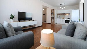 Ein modernes Wohnzimmer mit einem Flachbildfernseher, grauen Sofas und einer Lampe.