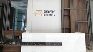 Ein Empfangsschalter mit Marmorplatte und Holzboden, umgeben von einem modernen Empfangsbereich mit weißer Wand und dem Logo von 'Singapore Residences'.
