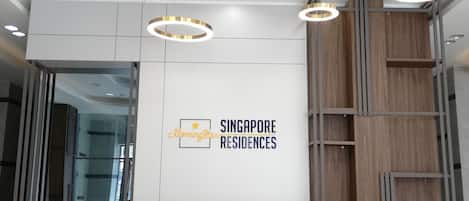 A reception desk with a marble top and a wooden base, surrounded by a modern reception area with a white wall and a logo for 'Singapore Residences'.