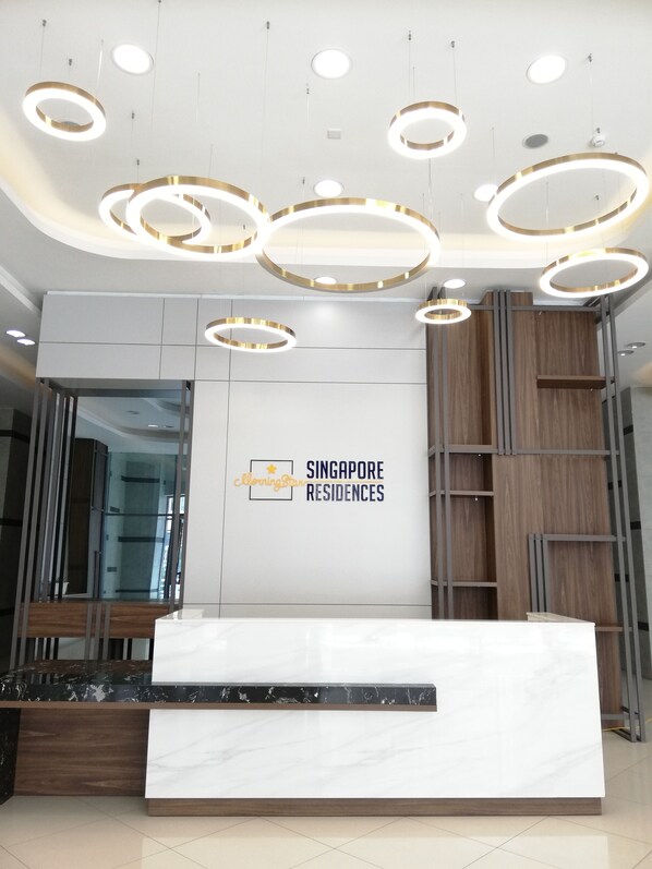 A reception desk with a marble top and a wooden base, surrounded by a modern reception area with a white wall and a logo for 'Singapore Residences'.