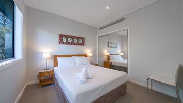 A hotel room with a large bed, two bedside tables with lamps, a mirror, and a window with a view of trees.