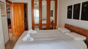 Habitación de hotel con una cama grande, armario de madera y un balcón con vistas.