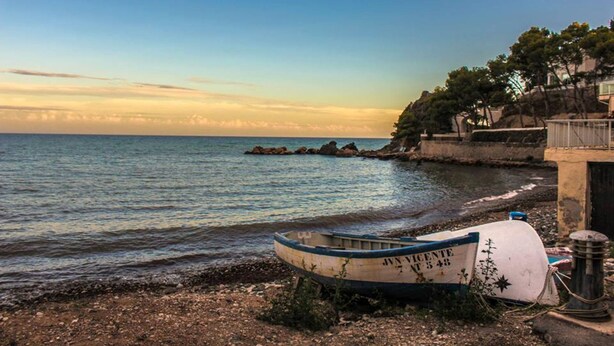 Un bote en una costa rocosa, cielo despejado y mar tranquilo.