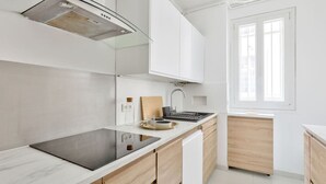 Et moderne køkken med hvide skabe, en sort induktionskogetop og en indbygget ovn.