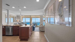 A spacious kitchen with a large island, a dining area with a view, and a living room with a large window overlooking the ocean. - Beach Club 1105 - 𝑪𝒐𝒂𝒔𝒕𝒂𝒍 𝑹𝒆𝒕𝒓𝒆𝒂𝒕 (Pensacola Beach)