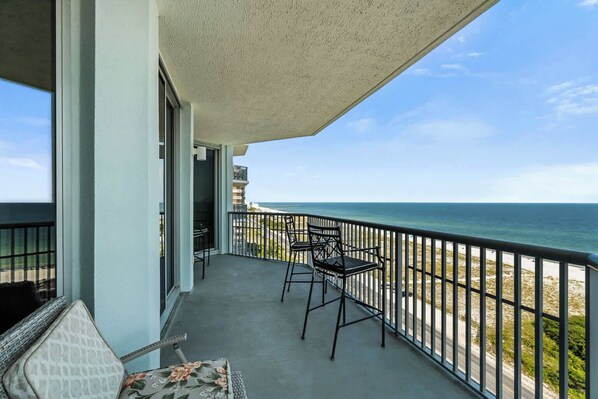 A balcony with a view of the ocean, two chairs, and a table.