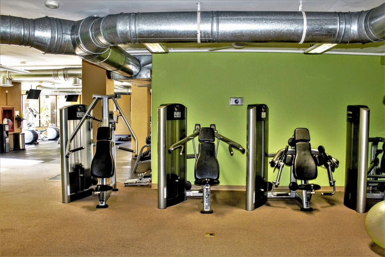Un gimnasio con equipo de ejercicio, una pared verde y un techo con conductos.