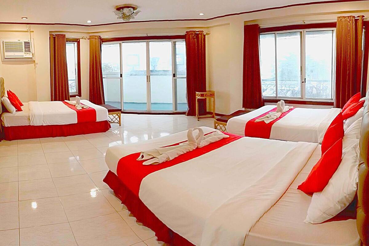 A hotel room with two beds, each with red and white bedding, a small table, and a view of the city through large windows.
