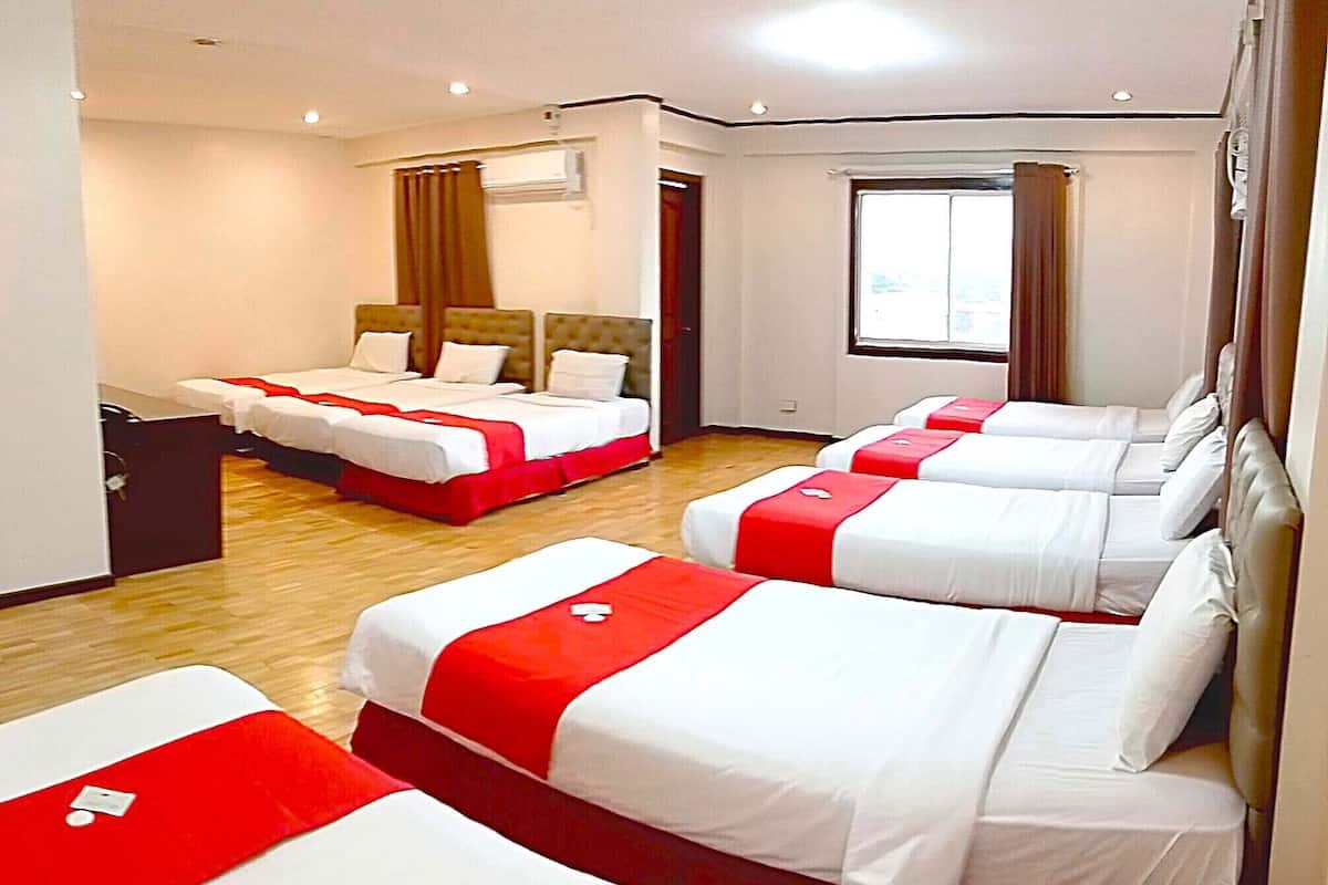 A hotel room with four beds arranged in a row, each with white bedding and red accents.