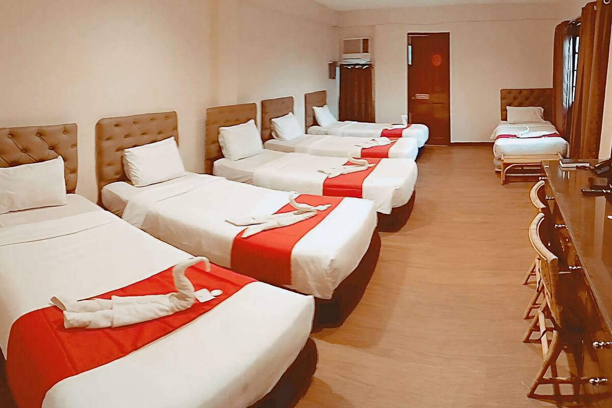 A hotel room with four beds arranged in a row, each with white bedding and red accents.