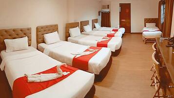 A hotel room with four beds arranged in a row, each with white bedding and red accents.
