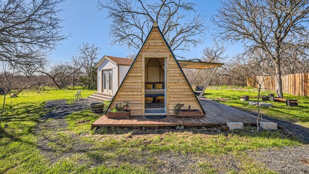Una cabana de fusta triangular amb una terrassa, una petita construcció annexa i una zona de jardí.