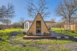 Une cabane triangulaire en bois dotée d’une terrasse, d’une petite structure attenante et d’un espace jardin.