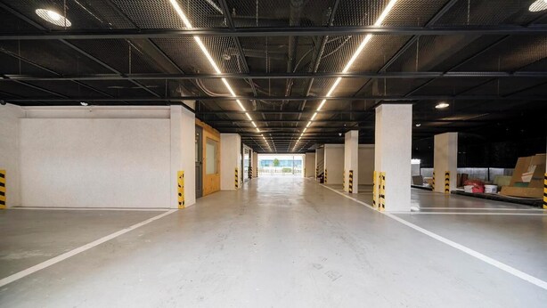 Un'ampia area di parcheggio interna con pavimenti in cemento e travi metalliche.