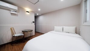 Una camera d'albergo moderna con un letto grande, un tavolino rotondo, una sedia e un condizionatore d'aria a parete.