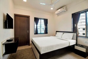 A bedroom with a bed, a TV, a desk, and a window with curtains.