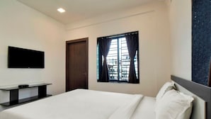 A hotel room with a bed, a flat-screen TV mounted on the wall, a window with curtains, and a door. - iROOMZ Growval Residency (Barasat)