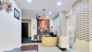 A reception area with a wooden desk, a large framed picture of a deity, and a patterned wall. - iROOMZ Growval Residency (Barasat)