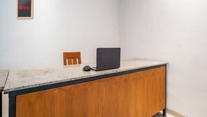 Een houten bureau met een laptop en muis, een kleine houten stoel, en een lijst met de letters 'OYO' op een witte muur.