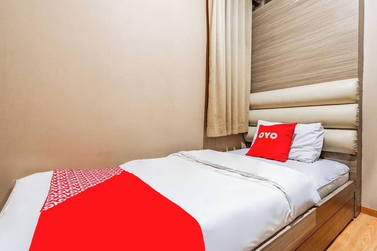 Una cama bien hecha con colcha roja y blanca, cabecera de madera y almohada roja con la palabra 