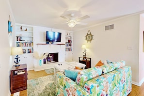 A living room with a white fireplace, a television, a ceiling fan, and a bookshelf.