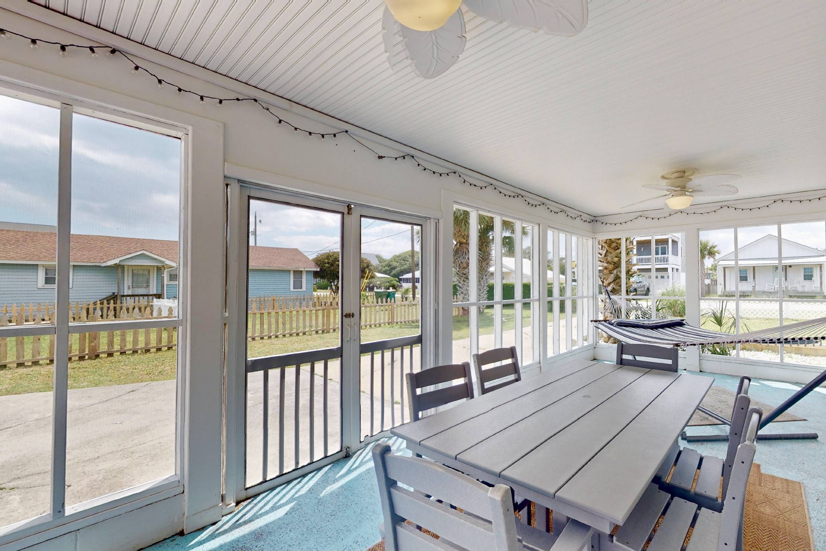 A covered patio with a table and chairs, large windows, and a hammock.