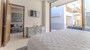 A bedroom with a large bed, a television on the wall, a dresser, and a view of the building's exterior through a glass door. - Penthouse in Romantic Zone! Pacifica 604 2BD Penthouse for rent in Old Town, Pue (Puerto Vallarta)