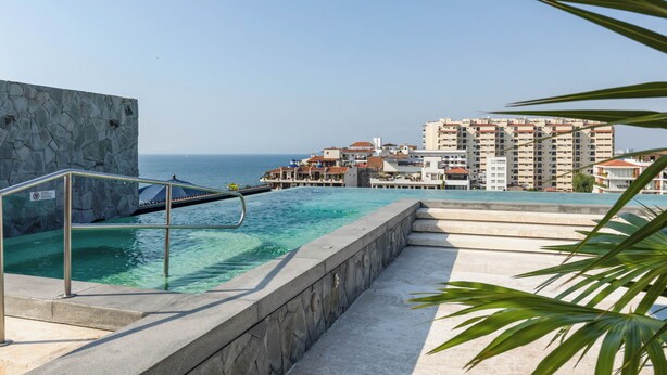 A swimming pool with a stone wall and metal railing, overlooking a coastal area with buildings and the sea. - Penthouse in Romantic Zone! Pacifica 604 2BD Penthouse for rent in Old Town, Pue (Puerto Vallarta)
