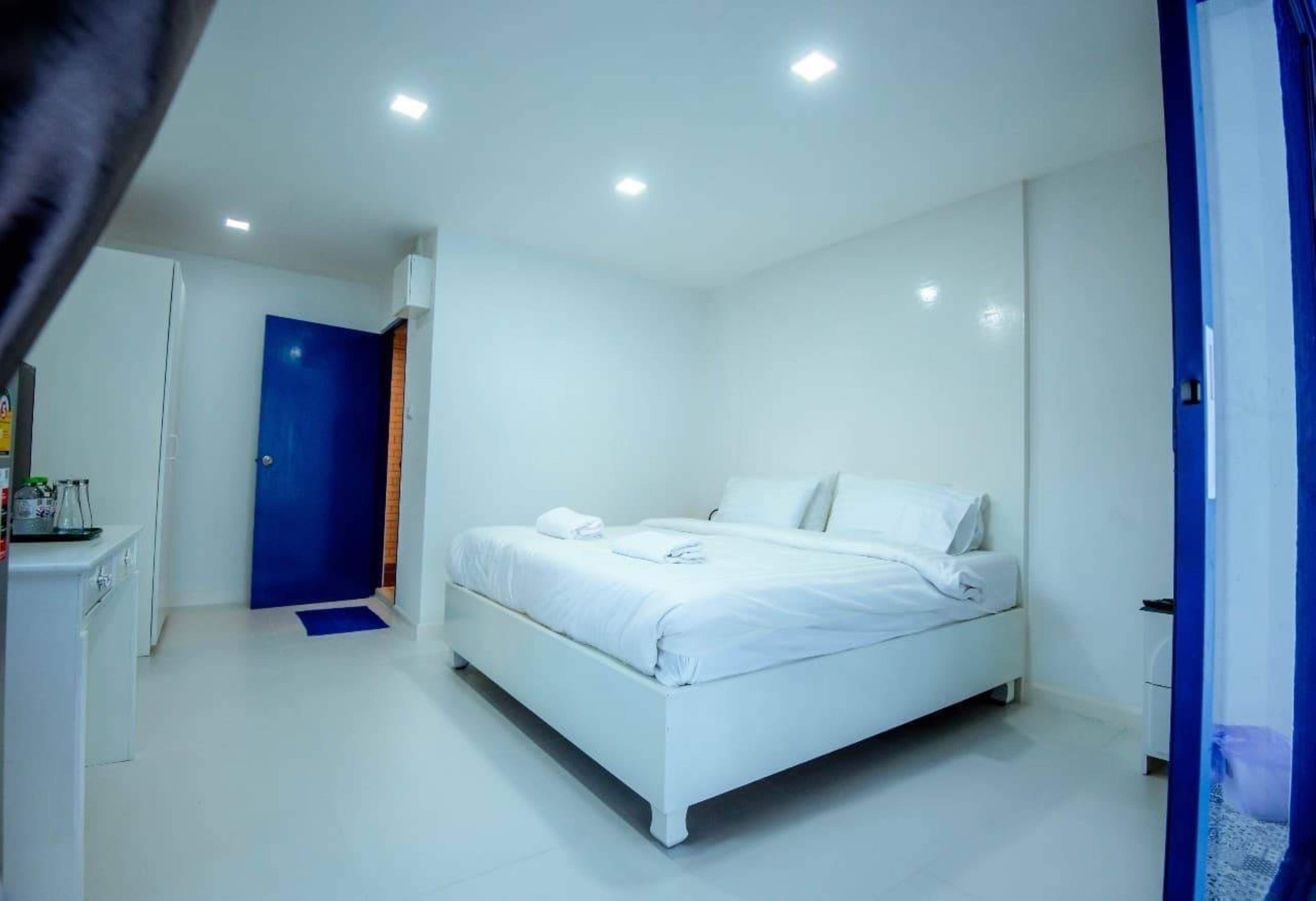 Habitación de hotel moderna con una decoración en blanco, una cama bien hecha, un escritorio pequeño y una puerta azul.