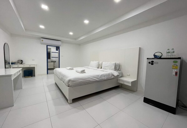 A modern hotel room with a large bed, a small desk, a mirror, and a refrigerator.