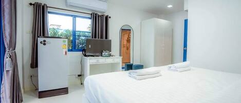A hotel room with a bed, a desk with a computer, an air conditioner, and a window with curtains.