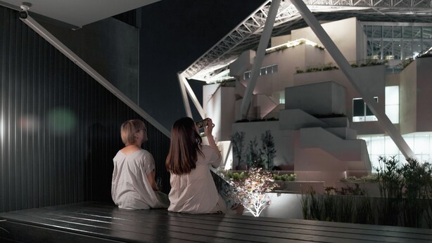 Two people sitting on a balcony overlooking a modern building with a unique architectural design. - J Youai House (Tainan)