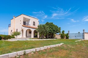 A two-story house with a balcony, a large tree in front, and a blue gate. - Villa Mattalia 500m From Sea (Manduria)