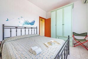 Un dormitorio con una cama, un armario verde, una silla plegable roja y un adhesivo en la pared.