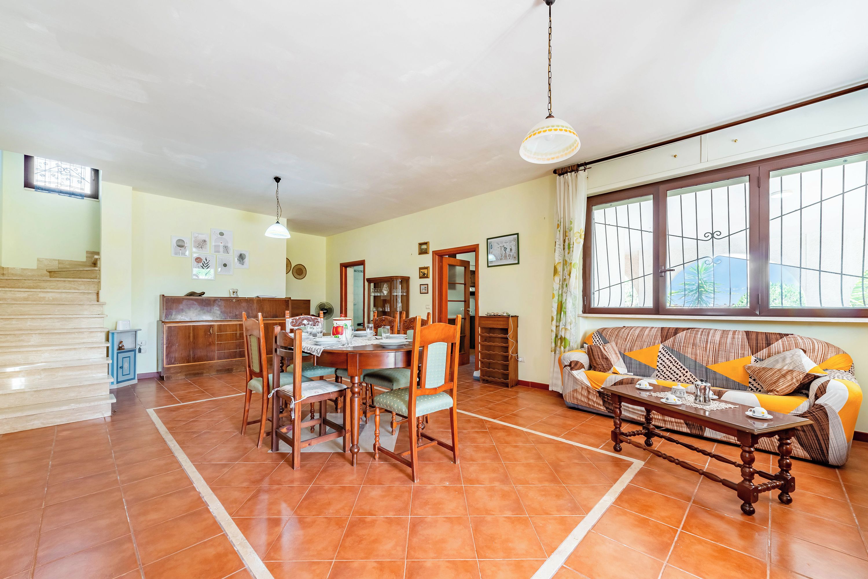 A spacious living area with a dining table, chairs, a sofa, and a staircase.