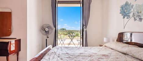 A bedroom with a bed, a fan, a piano, and a view of the outdoors.